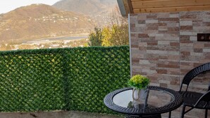 Un patio con una mesa redonda y sillas, una planta en maceta, y vistas a montañas y un río.