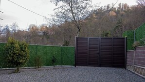 Un área cercada con camino de grava, seto verde y un árbol.