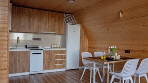 Moderni keittiö, jossa on puiset kaapit, valkoinen astianpesukone ja jääkaappi. Keittiössä on myös ruokailutila, jossa on puinen pöytä ja valkoiset tuolit.