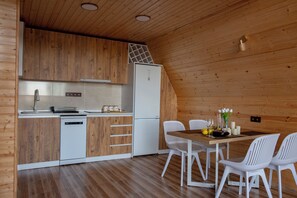 Een moderne keuken met houten kasten, een witte vaatwasser en een koelkast. Er is een eethoek met een houten tafel en witte stoelen.