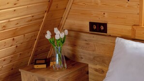 Habitación de cabaña de madera con cama, mesita de noche con un florero y cabecera de madera.