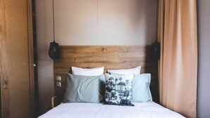 Ein Bett mit weißer Bettwäsche, einem Holzkopfende und zwei Kissen mit tropischem Muster.
