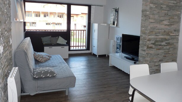 Una sala moderna con un sofá gris, un televisor de pantalla plana, una mesa de comedor y una pared de acento de piedra.