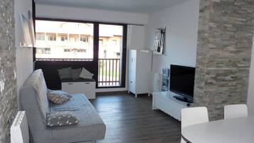 Un salon moderne avec un canapé gris, un téléviseur à écran plat, une table à manger et un mur décoratif en pierre.