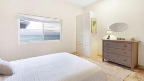 Un dormitorio con cama, cómoda, espejo y ventana con vista al mar.