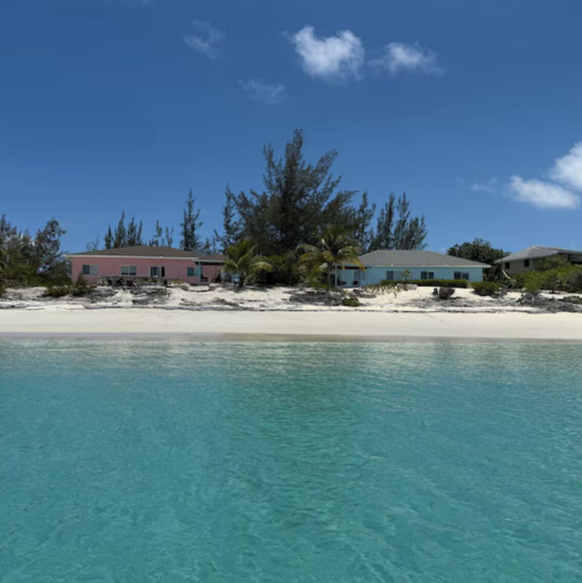 A beachfront property with a clear view of the ocean, a sandy beach, and several buildings.