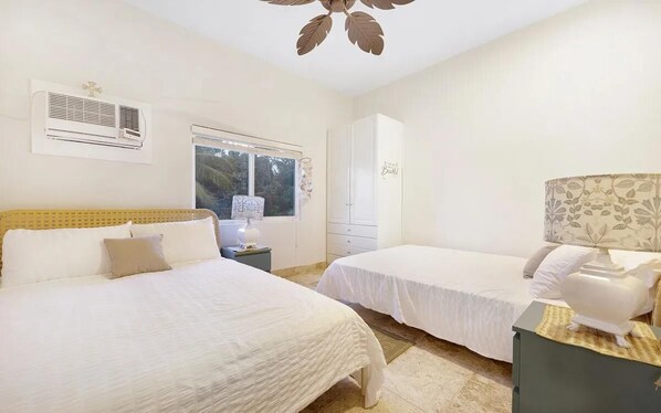 A bedroom with two beds, a window, an air conditioning unit, and a wardrobe.