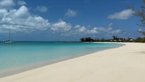 Una playa con agua turquesa cristalina, una orilla arenosa y vegetación escasa.