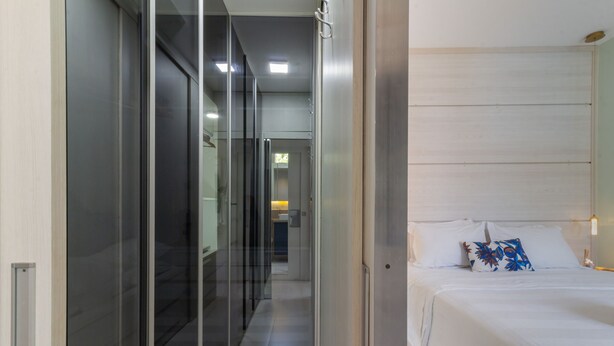 A modern hotel room with a glass partition, a neatly made bed with white bedding and a decorative pillow, and a visible bathroom in the background. - Apartment on Gigoia Island Gigoia Class (Rio de Janeiro)