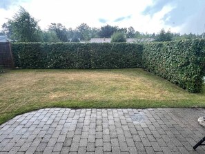 Eine gepflasterte Terrasse mit Rasenfläche und einer dichten Hecke.