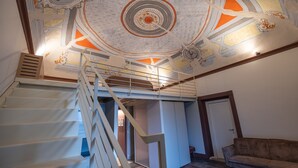 Eine Treppe führt zu einer zweiten Etage mit kunstvollen Deckenverzierungen, im Vordergrund steht eine Couch.