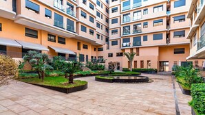 A multi-story residential building with a courtyard featuring tiled flooring, palm trees, and a central water feature. - Quiet & Secure Apt - Fast WiFi - Central Area (Marrakesh)