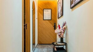 A hallway with a wooden door, a welcome sign, a framed picture, and a small table with a vase of flowers. - Quiet & Secure Apt - Fast WiFi - Central Area (Marrakesh)