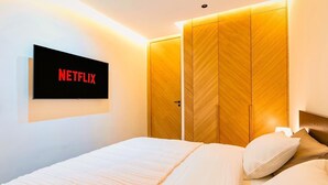 A hotel room with a bed, a TV mounted on the wall displaying 'NETFLIX', and a wooden wardrobe. - Quiet & Secure Apt - Fast WiFi - Central Area (Marrakesh)