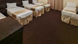 Ein Hotelzimmer mit vier Einzelbetten, einem Schreibtisch und einem großen Fenster mit Vorhängen.