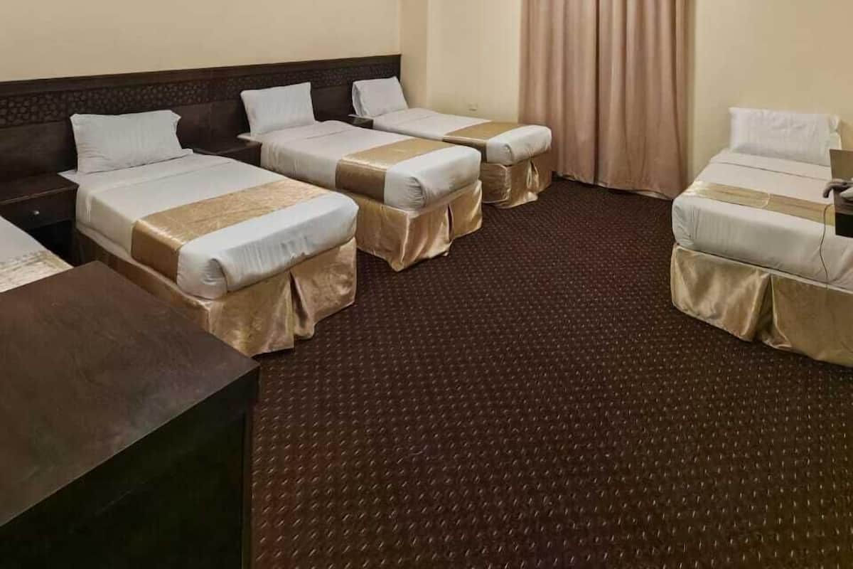 A hotel room with four single beds, a desk, and a large window with curtains.