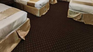 Ein Hotelzimmer mit drei Einzelbetten, einem dunklen Teppich, einer Deckenleuchte und einem Vorhangfenster.