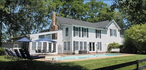 Ein zweistöckiges Haus mit Swimmingpool, Außenbereich zum Sitzen und einem großen Baum im Hintergrund.