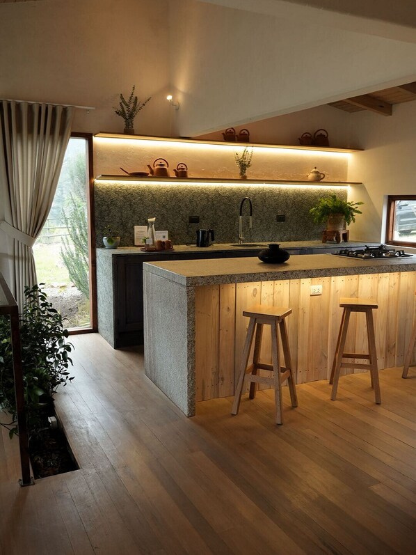 A modern kitchen with a central island, wooden stools, and a stone backsplash. - Wayarumi (Tinco)