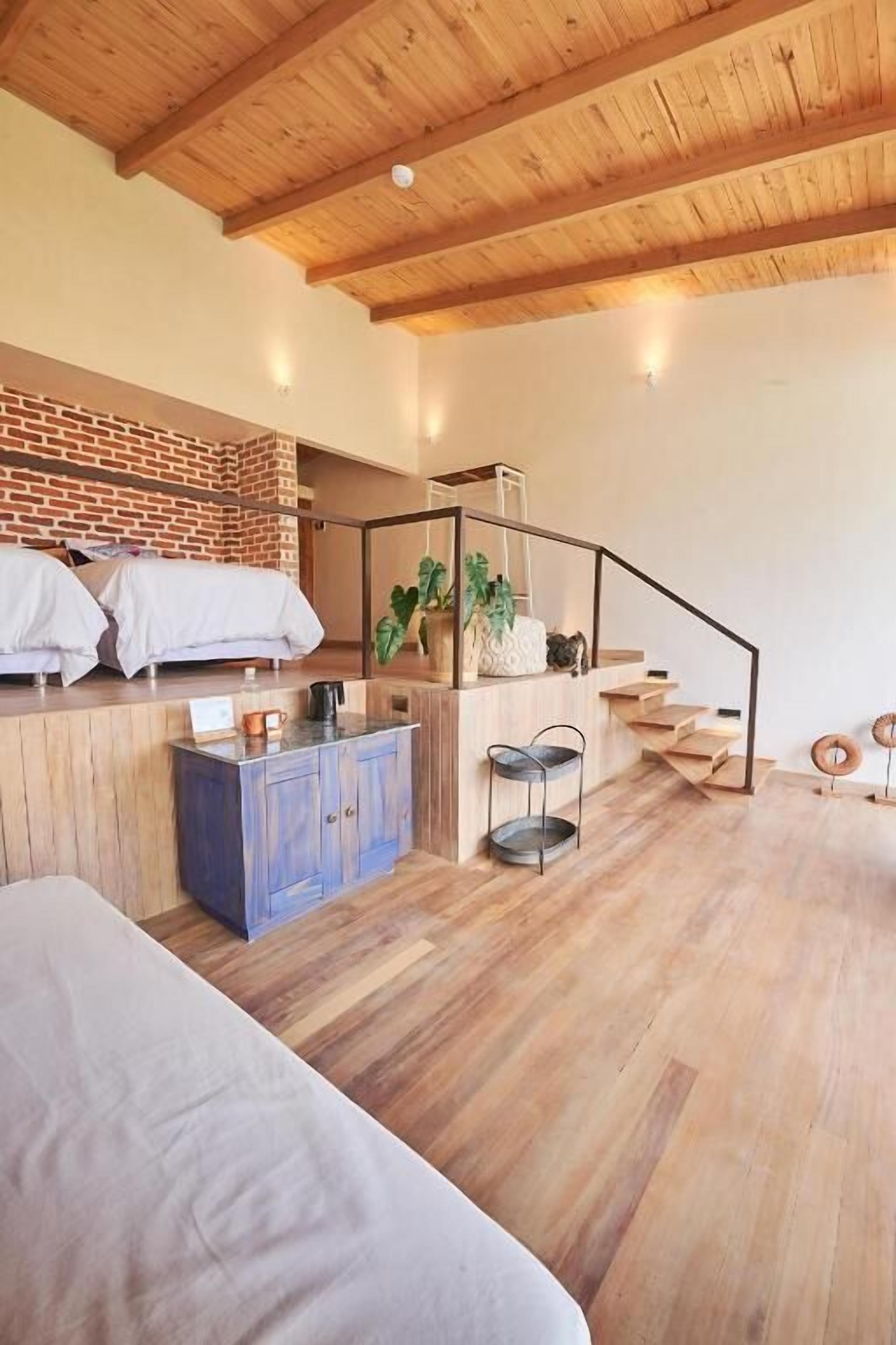 A modern hotel room with a wooden ceiling, a brick wall, a staircase, and a bed.