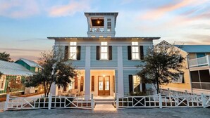 A two-story building with a central entrance, a small balcony on the upper floor, and a white picket fence in front. - Sea La Vie Seaside Main House (Santa Rosa Beach)