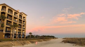 Hotel a peu de platja amb diversos balcons, sorra daurada i cel serè.