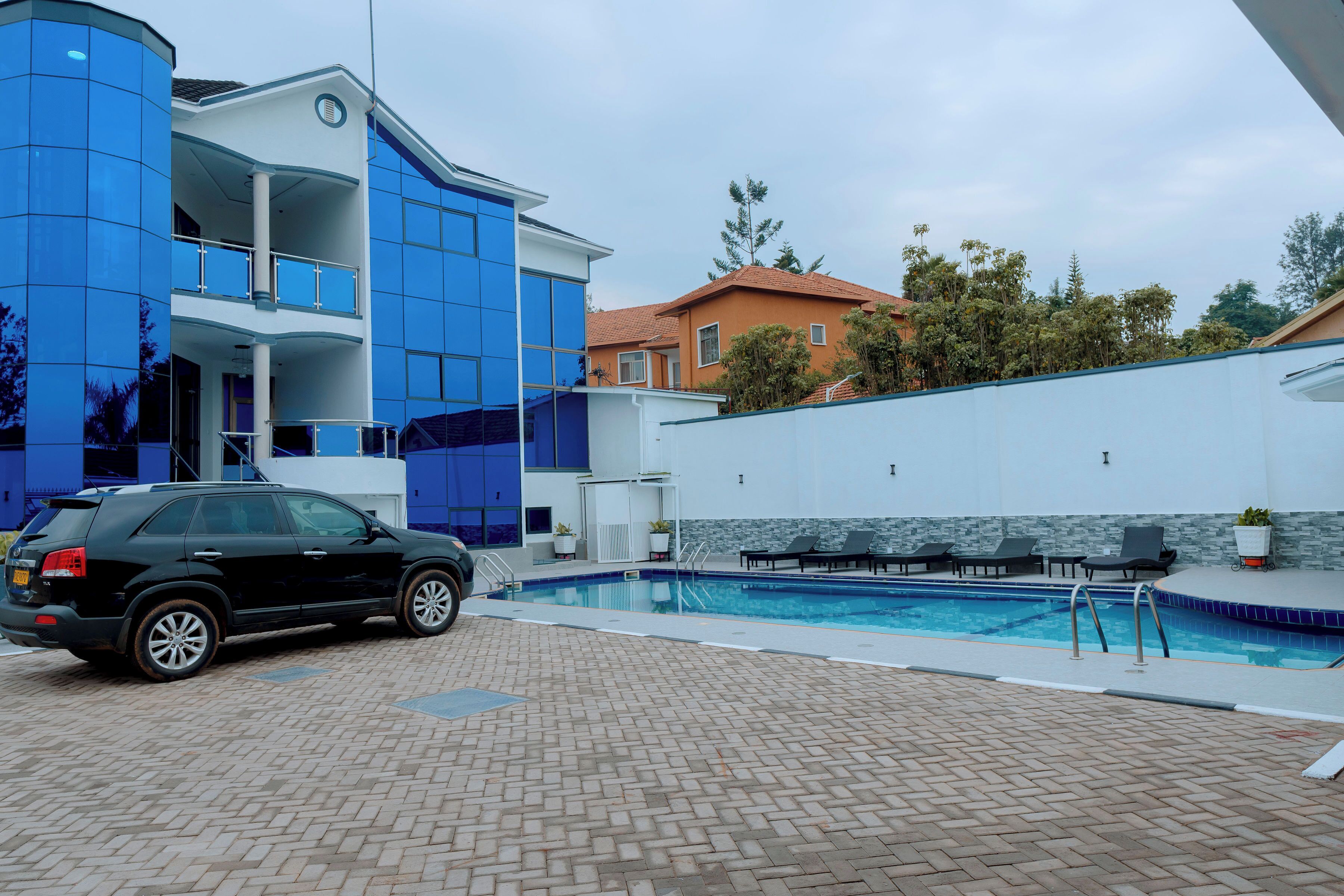 A modern building with a swimming pool, a car parked in front, and a brick patio area.