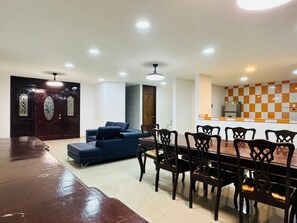 A spacious living room with a dark wooden dining table and chairs, a blue sofa, and a kitchen area with a checkered backsplash. - Villa Casa Cocos private for 10 people in Tulum (Tulum)