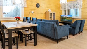 A cozy cabin interior with a wooden interior, a dining table with chairs, a sofa, a television, and a clock on the wall. - Joutsenranta by Interhome (Tuusniemi)