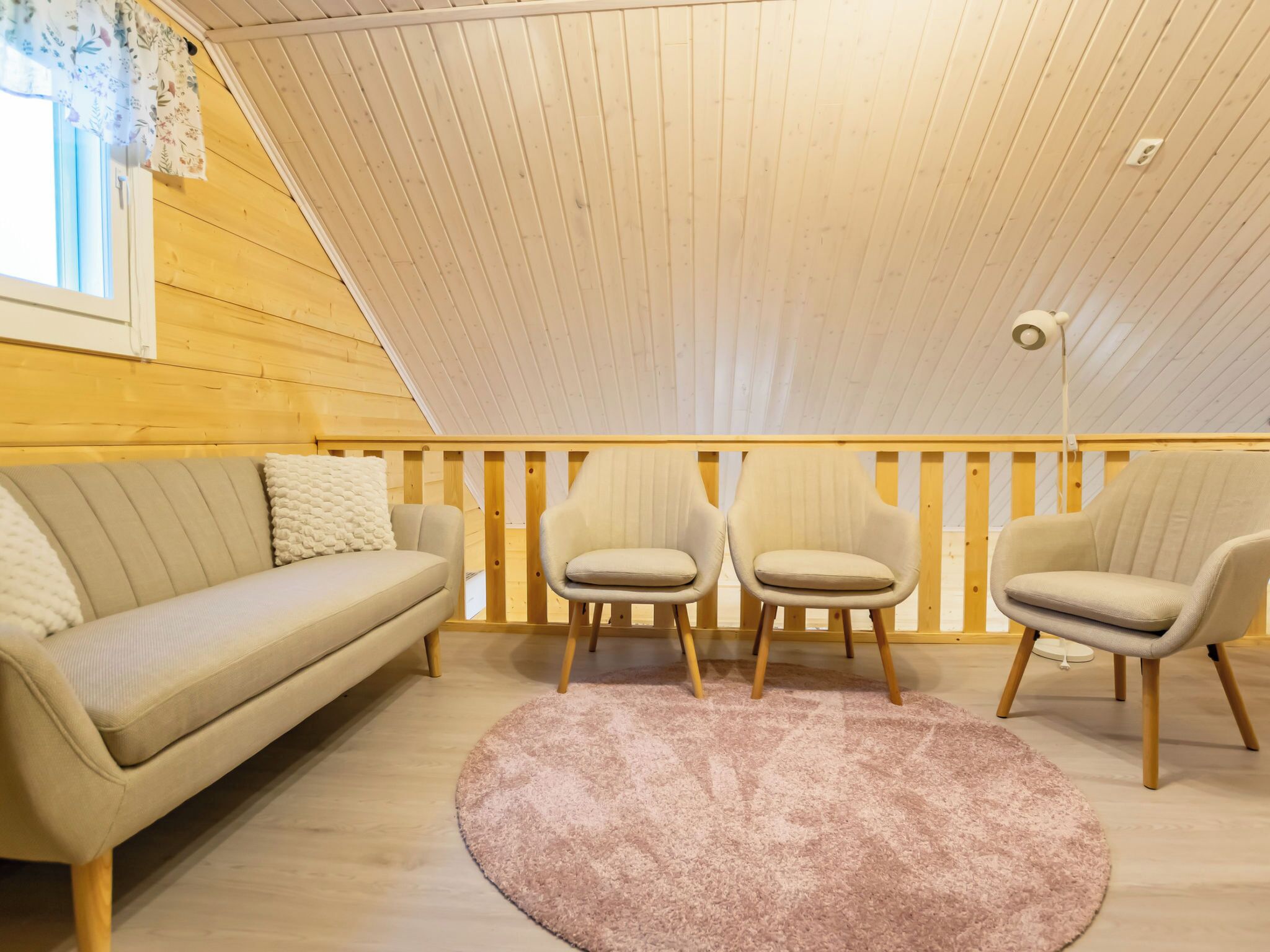 Une pièce chaleureuse avec un plafond en bois, un canapé beige, deux fauteuils et un tapis rose.