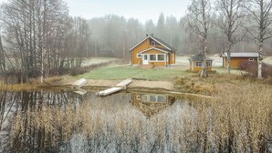 A rustic cabin with a large window, surrounded by a pond and dense trees. - Joutsenranta by Interhome (Tuusniemi)