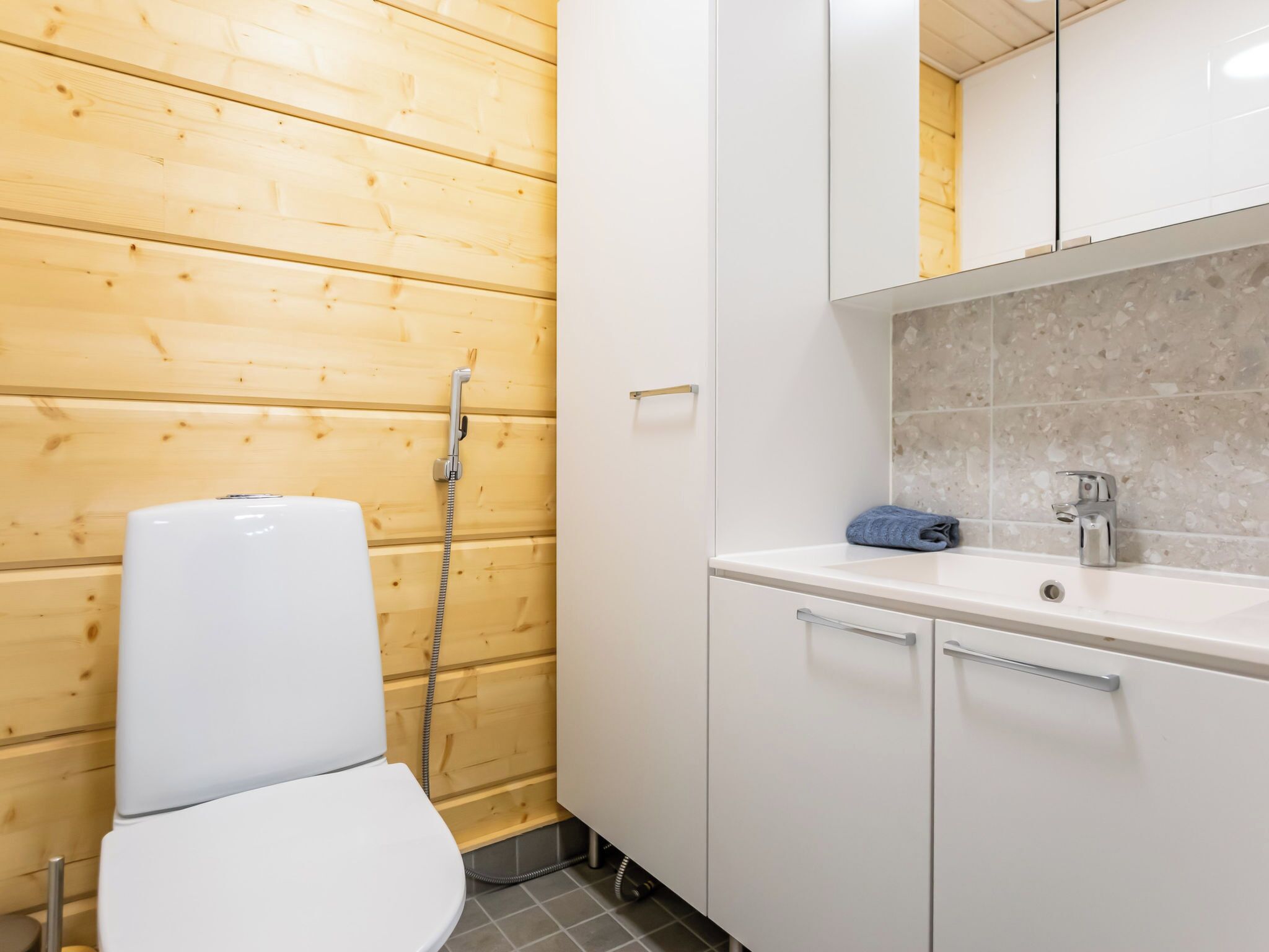 A bathroom with a wooden wall, a white toilet, a sink with a mirror, and a shower.