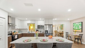 A modern kitchen with white cabinets, stainless steel appliances, and a central island with bar stools. - Backyard Paradise • Sleeps 14 • Arcade Games • Spa (Bradenton)