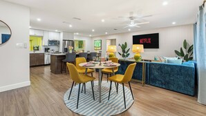 A modern living room with a dining area, a kitchen, and a TV displaying 'NETFLIX'. - Backyard Paradise • Sleeps 14 • Arcade Games • Spa (Bradenton)
