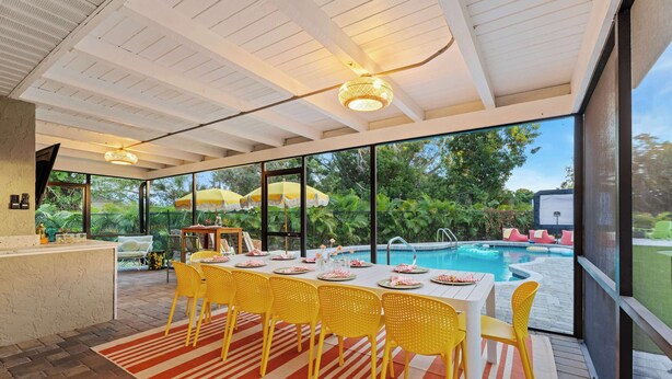 A dining area with a pool view, yellow chairs, and a table set for a meal. - Backyard Paradise • Sleeps 14 • Arcade Games • Spa (Bradenton)
