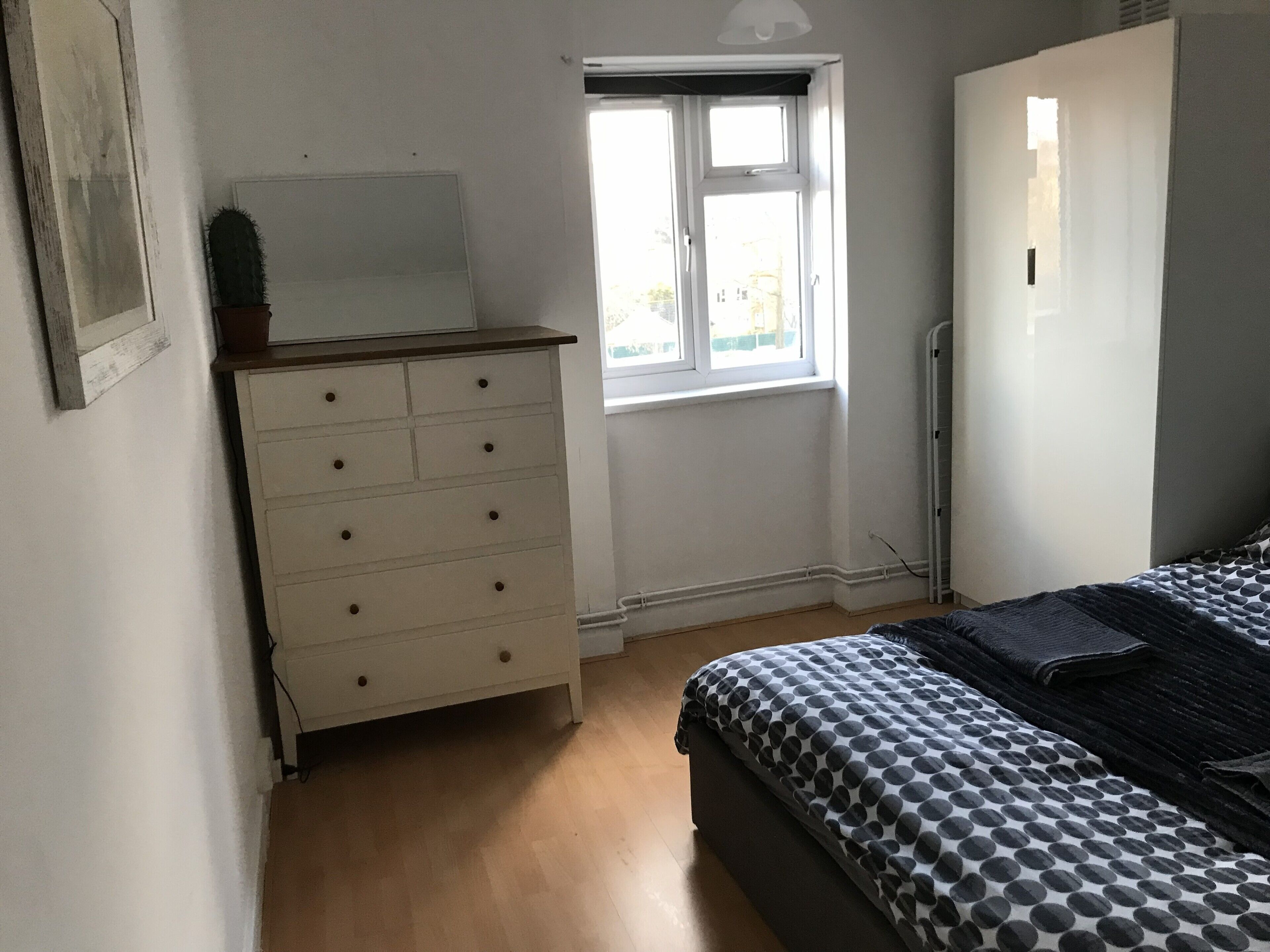Un dormitorio con cama, cómoda, ventana y radiador.