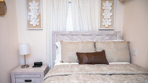 Une chambre à coucher avec un lit, une table de chevet dotée d’une lampe et d’une horloge, et des œuvres d’art murales.