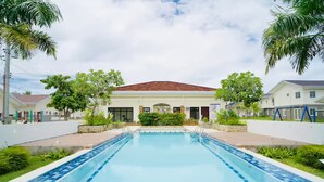 Une piscine dotée d’une terrasse carrelée, entourée de verdure et bordée d’un bâtiment au toit rouge.
