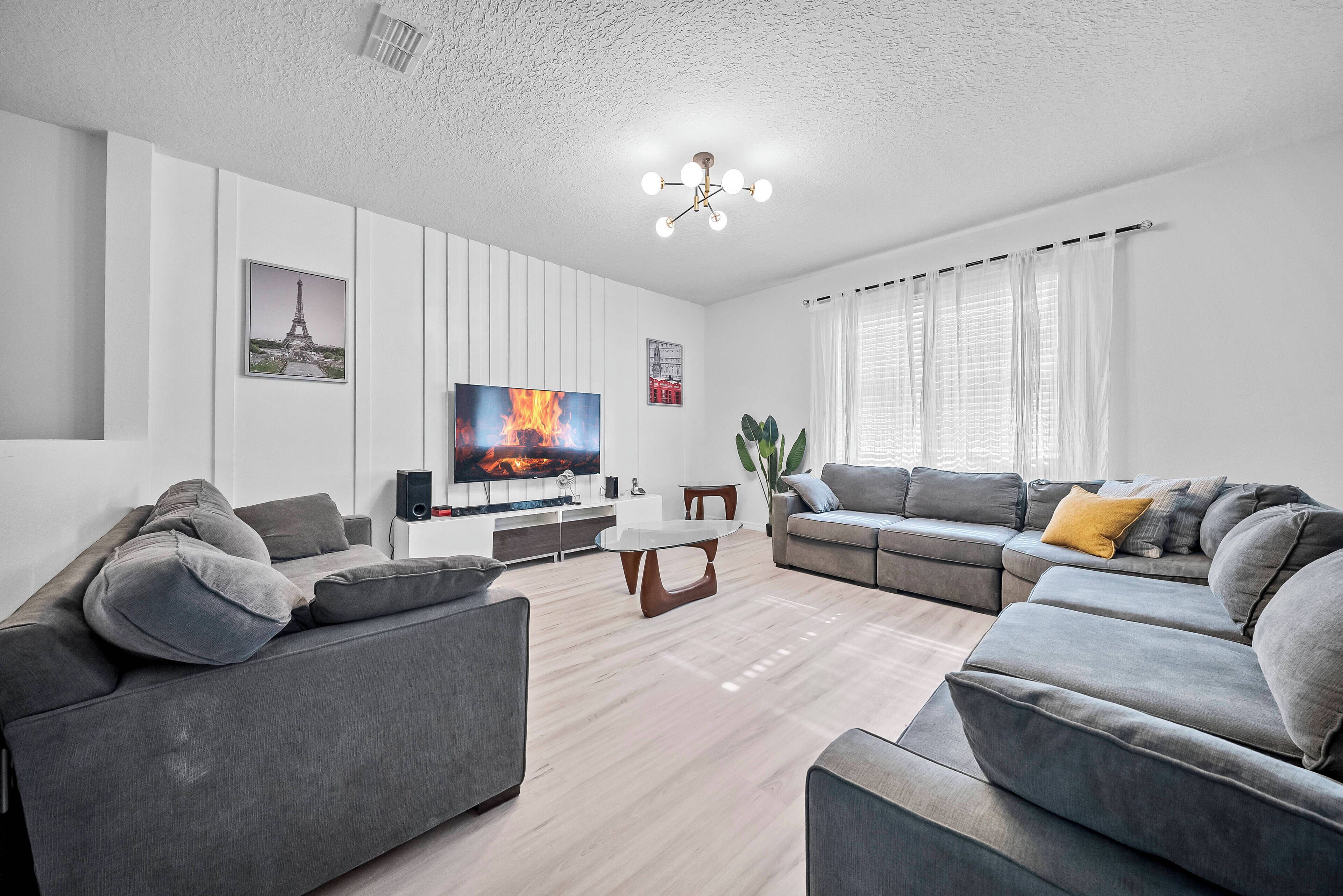 Een moderne woonkamer met een hoekbank, een flatscreen televisie en een eettafel.