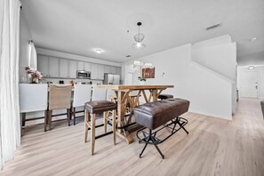 A modern kitchen with white cabinets, a wooden dining table, and a bench. - 8BR house with private pool in Crystal Cove (Kissimmee)