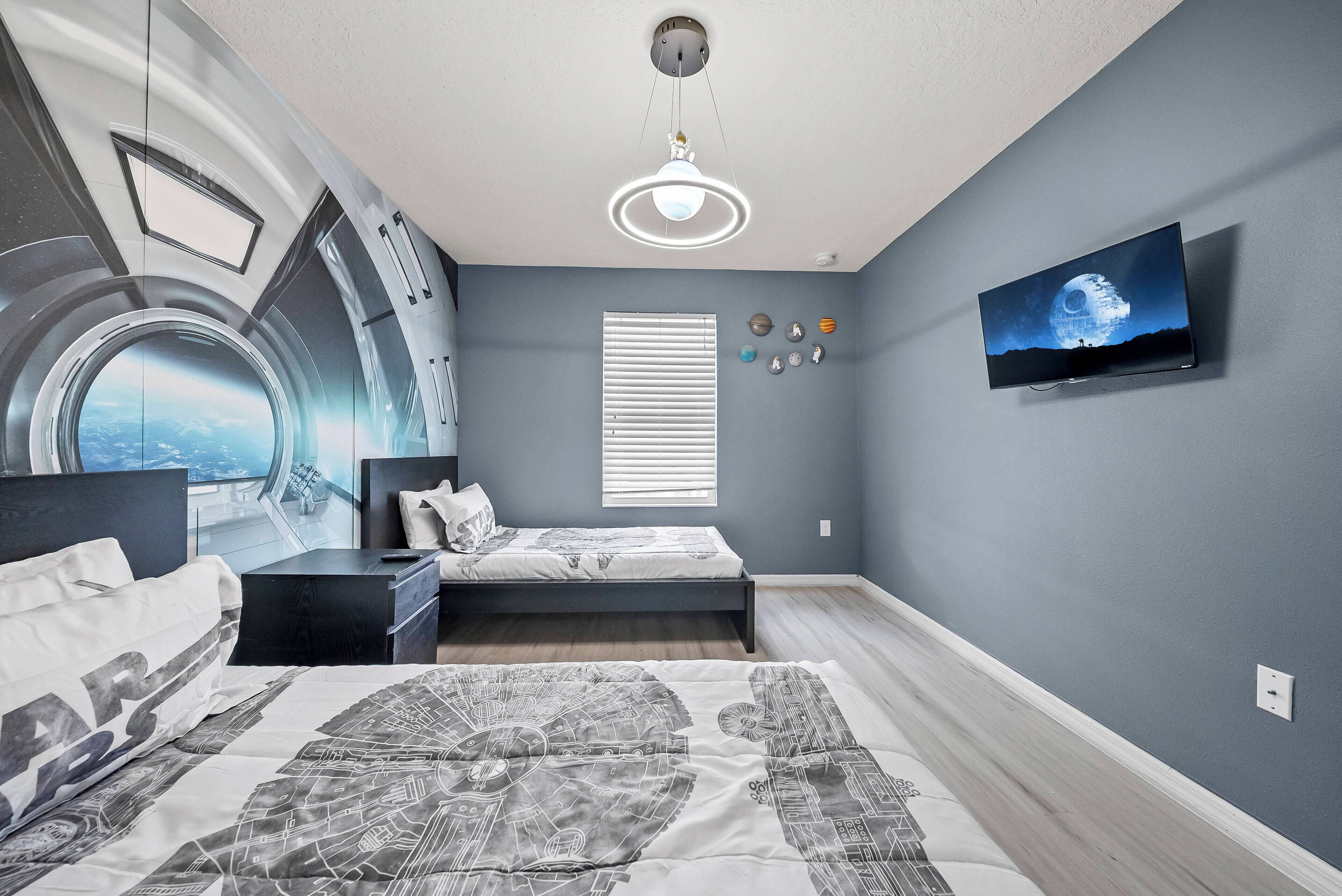 Une chambre moderne avec un lit, un bureau, une télévision et une fenêtre équipée de stores.