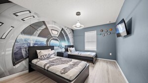 Een slaapkamer met een wanddecoratie in een boog, een bed, nachtkastje, een televisie en een raam met jaloezieën.