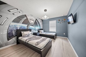 Ein Schlafzimmer mit Wandmalerei, einem Bett, einem Nachttisch, einem Fernseher und einem Fenster mit Jalousien.