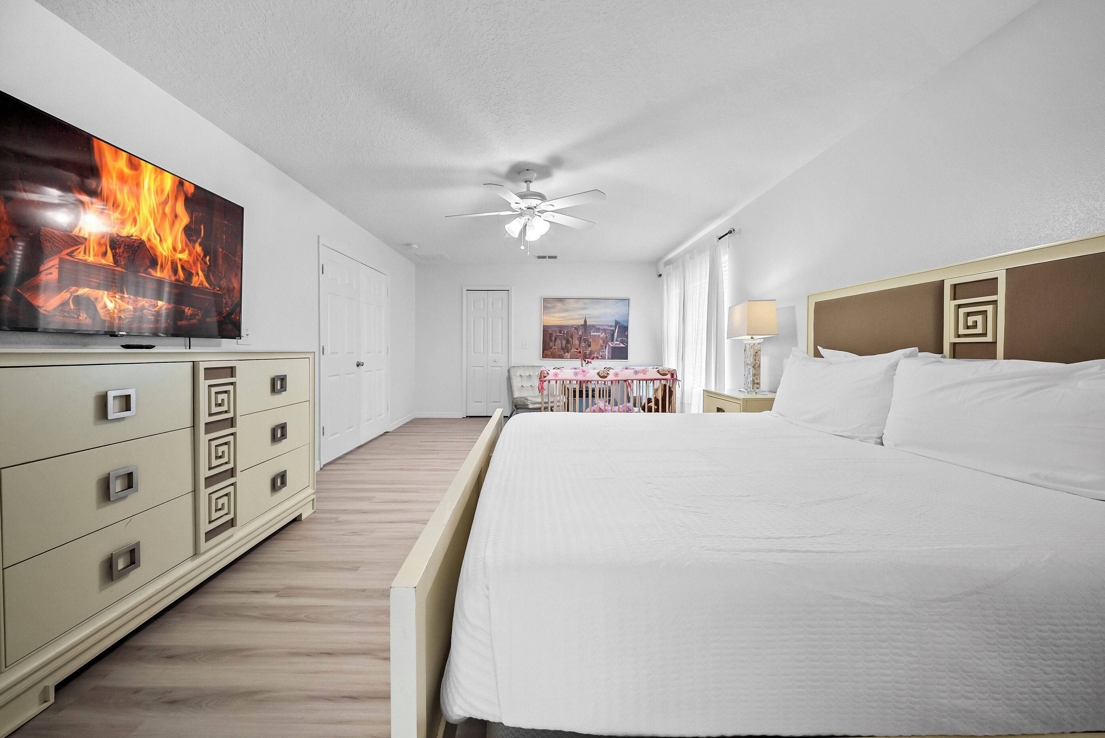 Ein Hotelzimmer mit einem großen Bett, einem Fernseher, einem Deckenventilator und Blick auf die Stadt durch das Fenster.