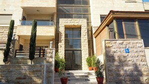 Un bâtiment moderne avec une façade en pierre, de nombreux balcons et des plantes en pot à l’entrée.