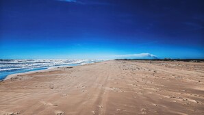 A wide sandy beach with footprints leading to the water, under a clear blue sky.