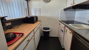 Eine kompakte Küche mit Mikrowelle, Toaster, Spüle und einer Uhr an der Wand.