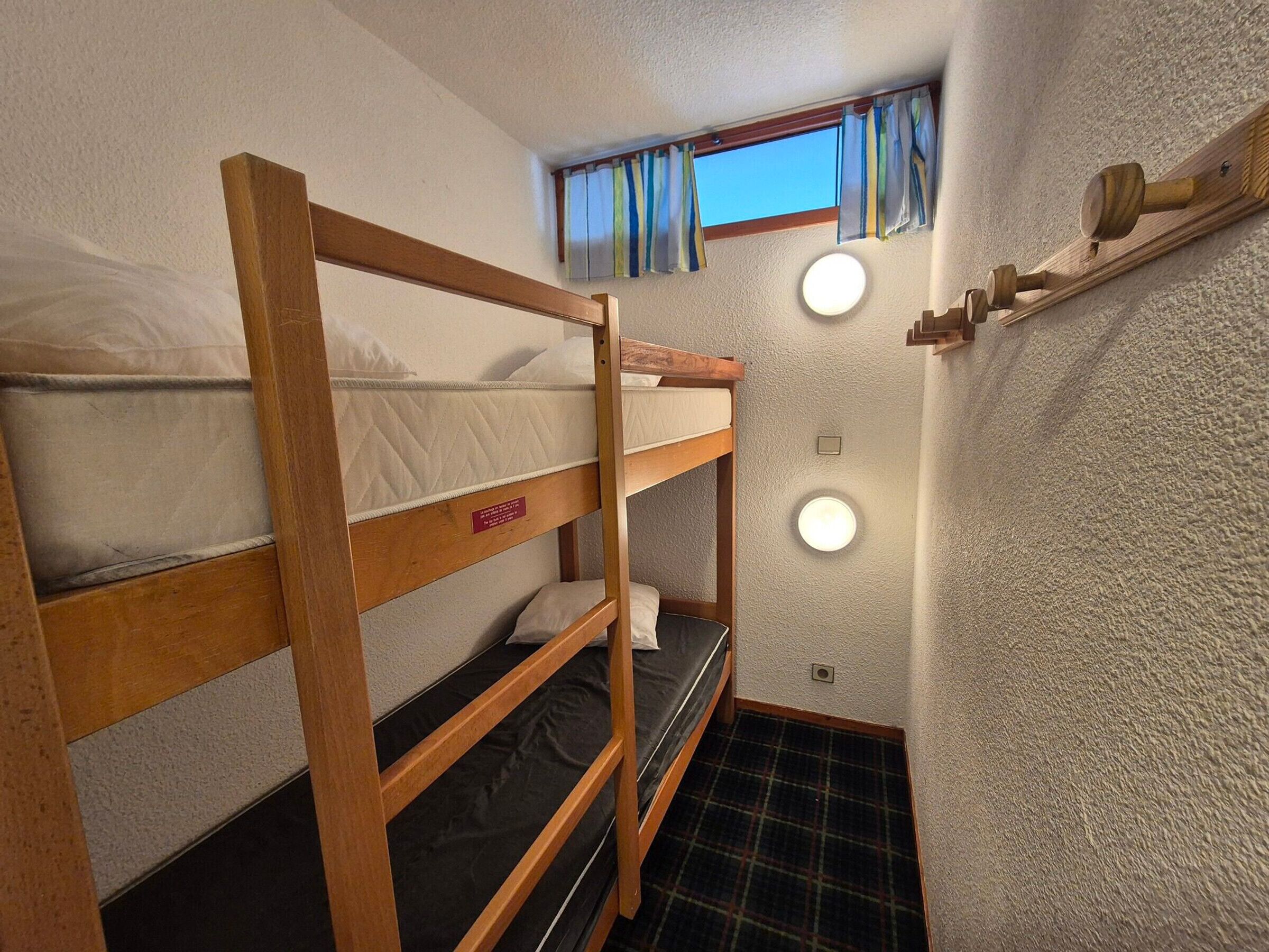 Een slaapkamer met een stapelbed, een raam, twee wandlampen en een houten plank met een hamer.
