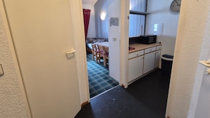 Ein schmaler Flur, der zu einem Schlafzimmer mit Bett und rotem Vorhang führt.