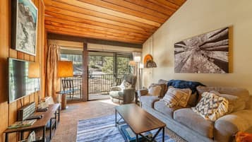 Un salon chaleureux avec un plafond en bois, un canapé, une table basse et un téléviseur.